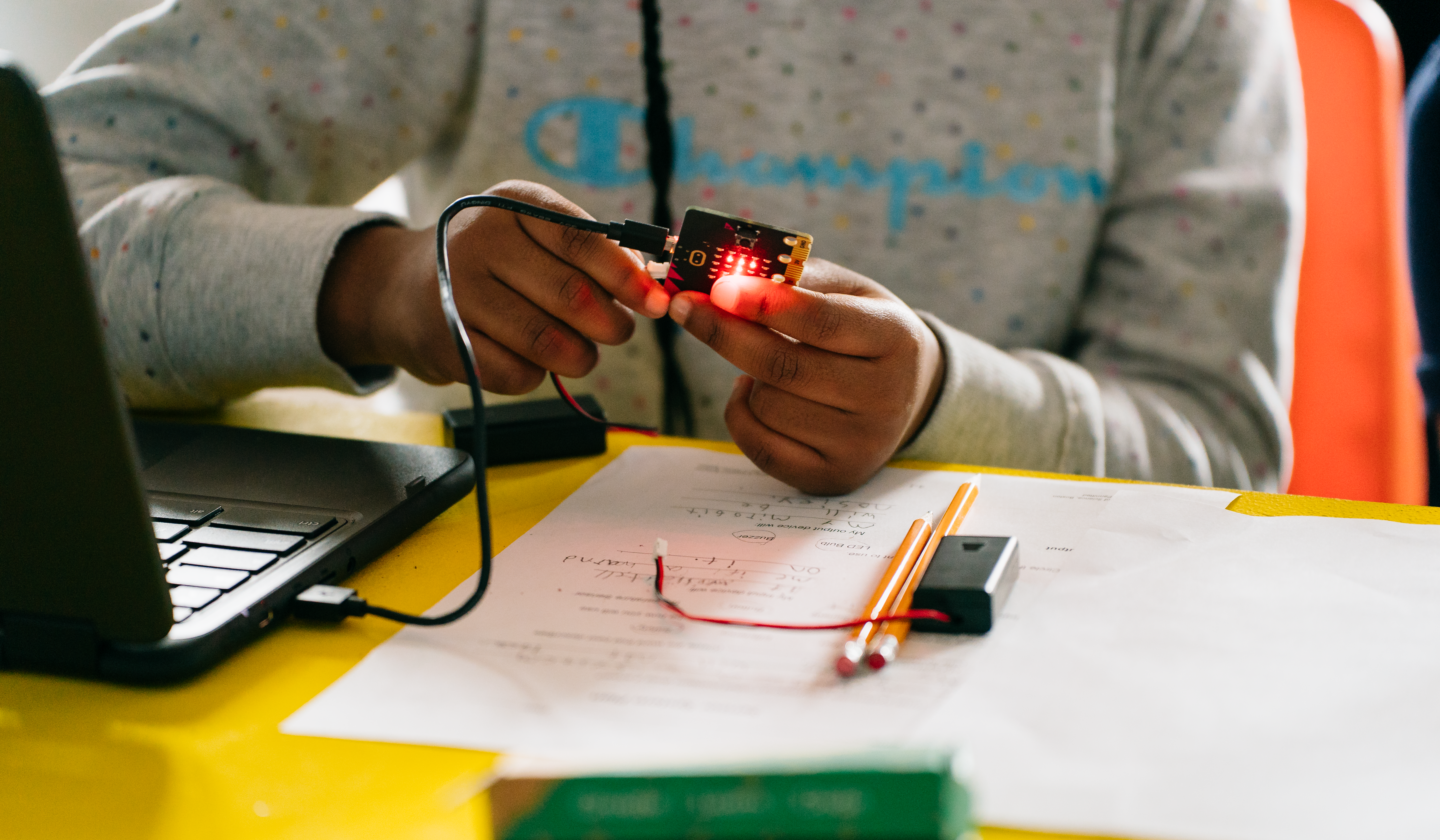 Two girls pouring into a glass vial and note pages.